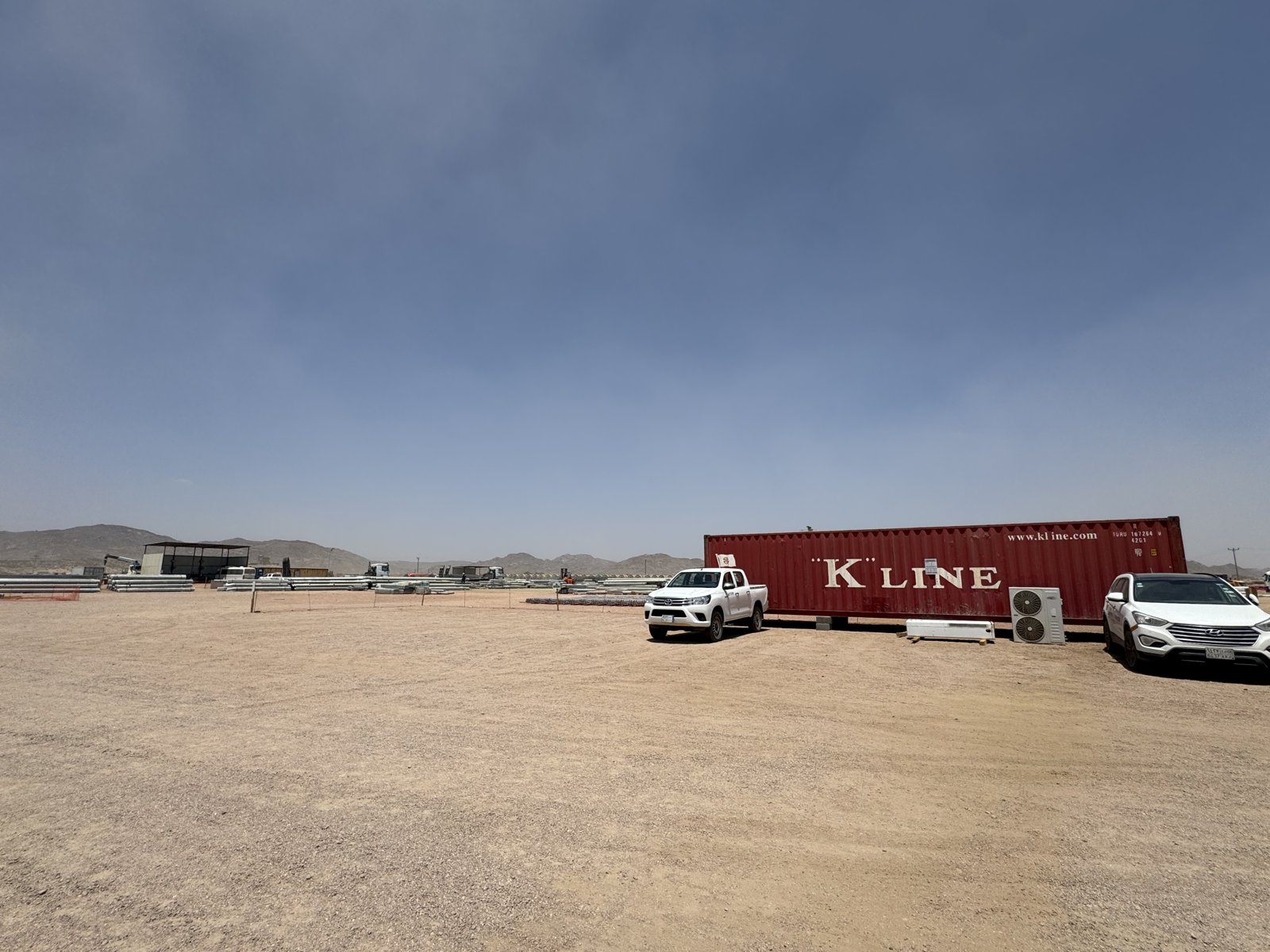An open site yard with stored materials, a shipping container and parked vehicles.
